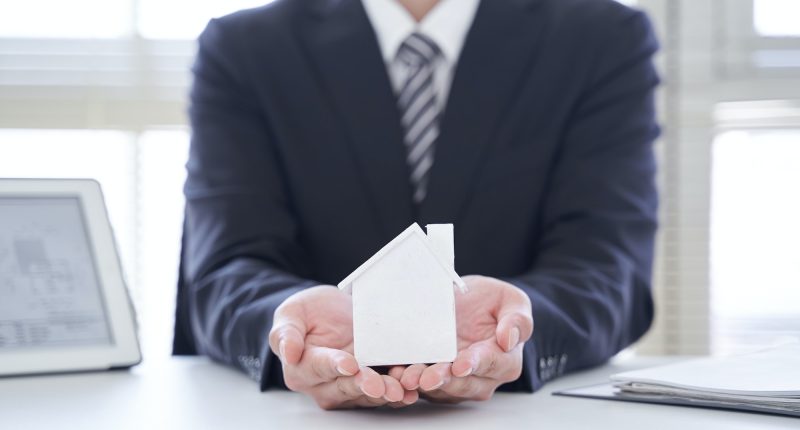 A Japanese male real estate salesman holding a house object